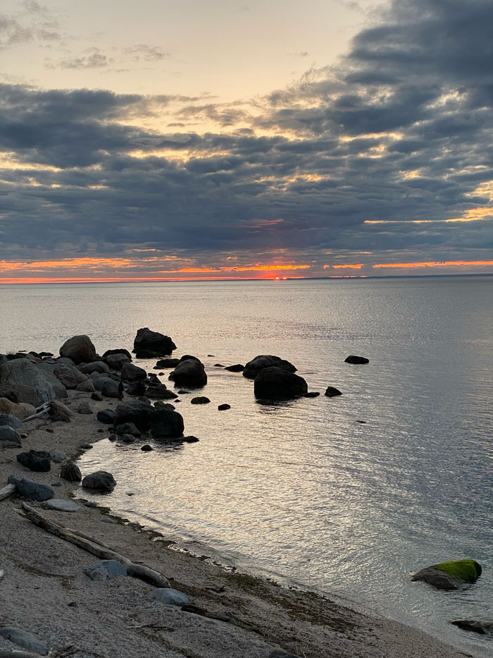 Dark rocks along a shoreline under a glowing sunset sky